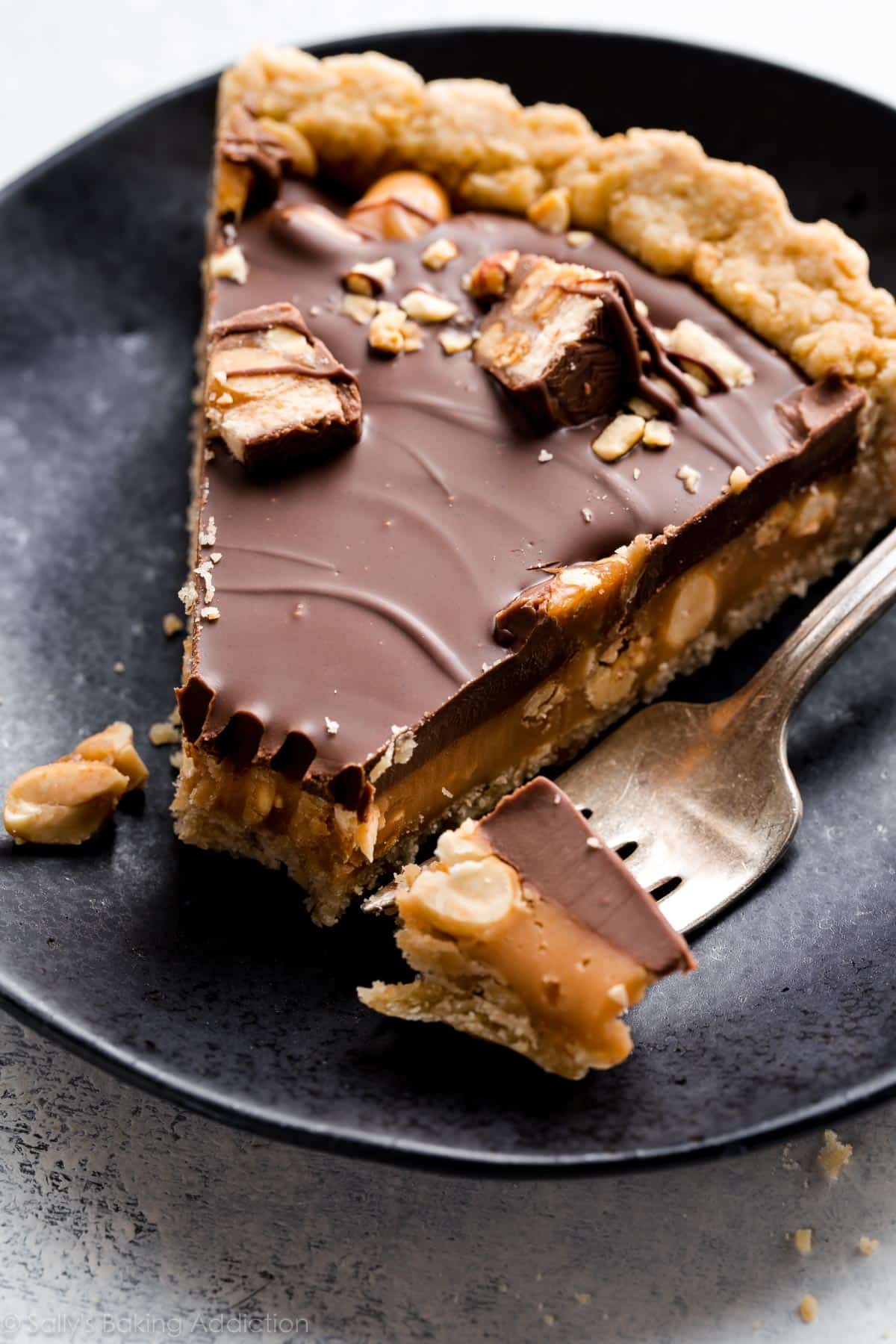 slice of Snickers caramel tart on a black plate with a fork