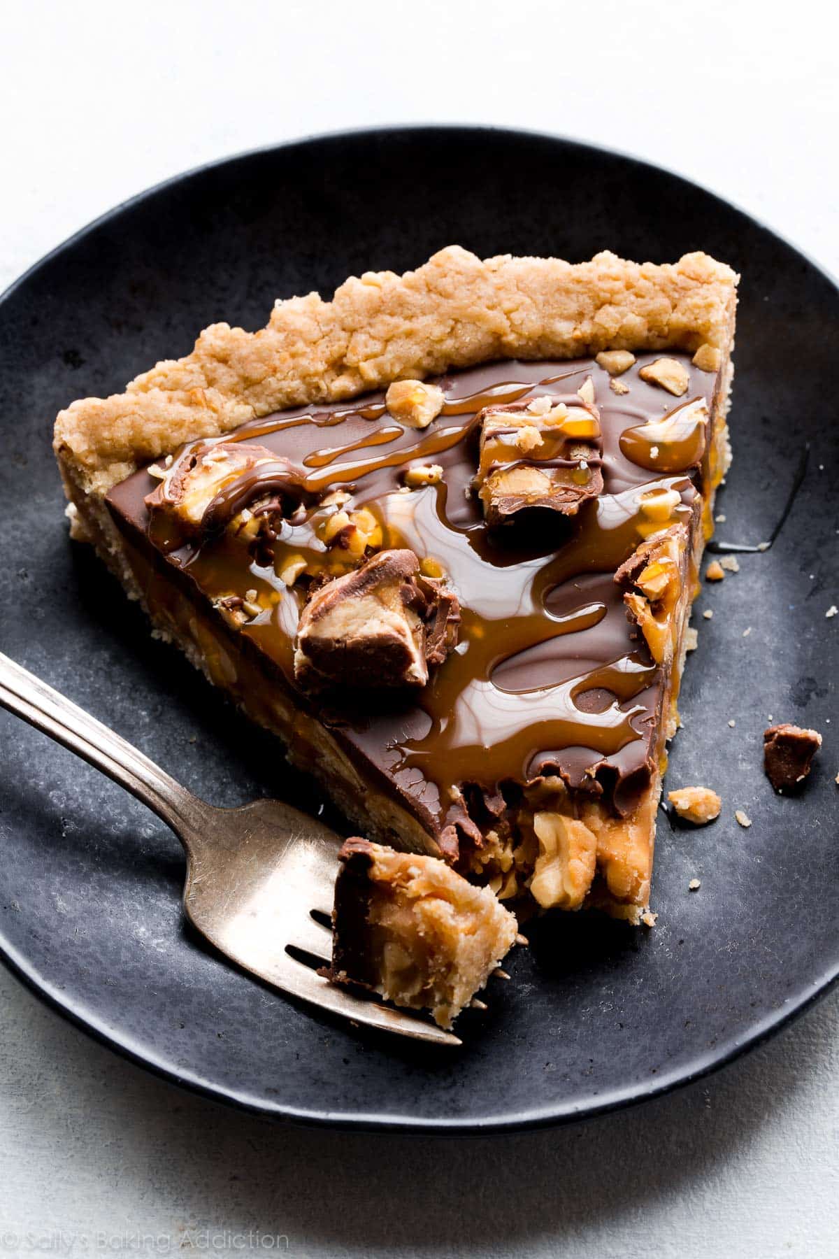 slice of Snickers caramel tart on a black plate with a fork