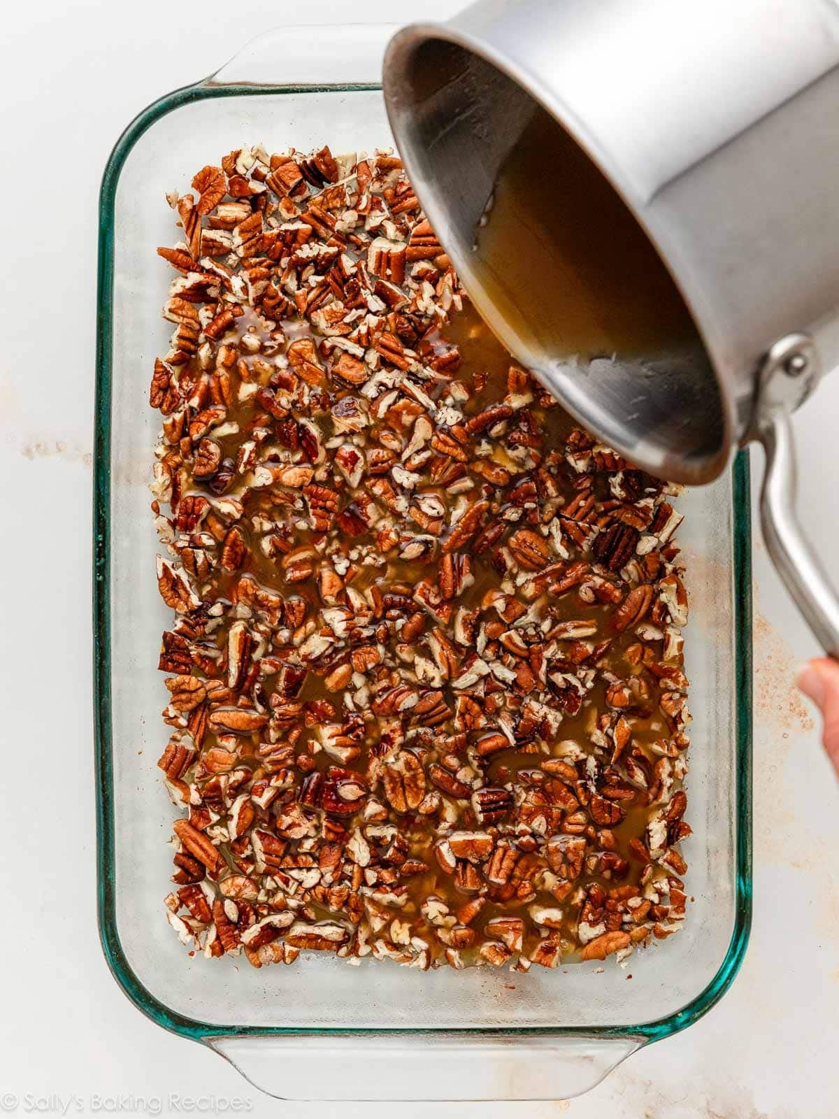 pouring caramel glaze over a pan of pecans.