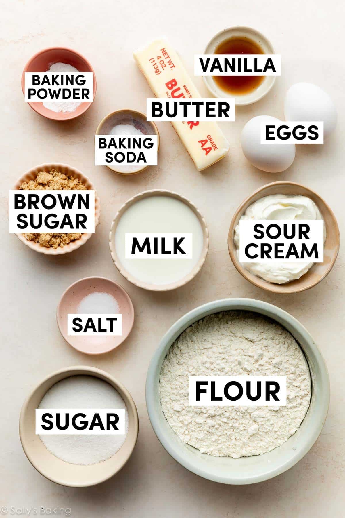 ingredients on beige surface including brown sugar, sour cream, flour, butter, vanilla, and eggs.