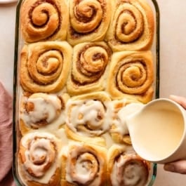 pouring orange icing on orange sweet rolls.