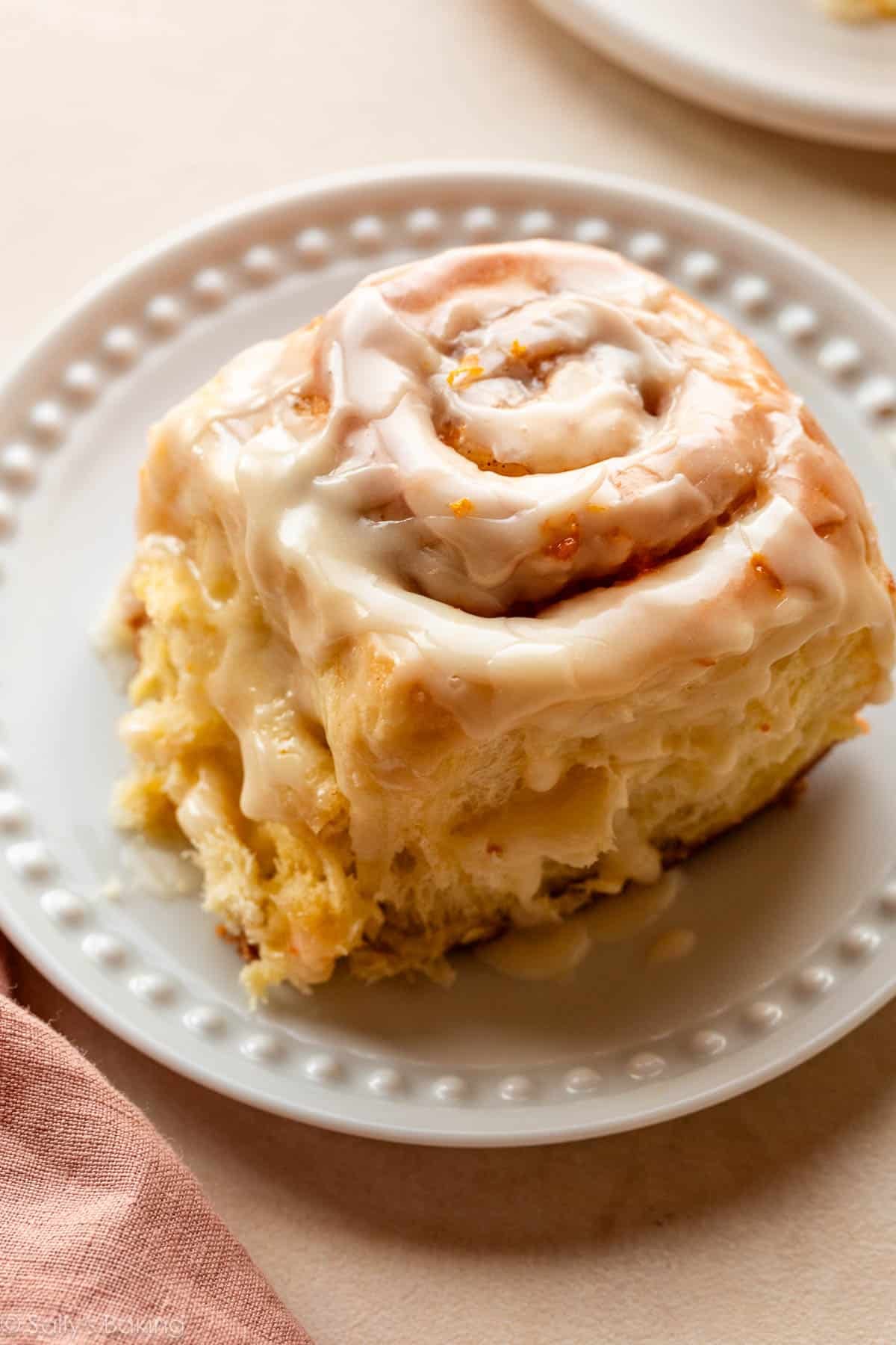 orange sweet cinnamon roll with icing on white plate.