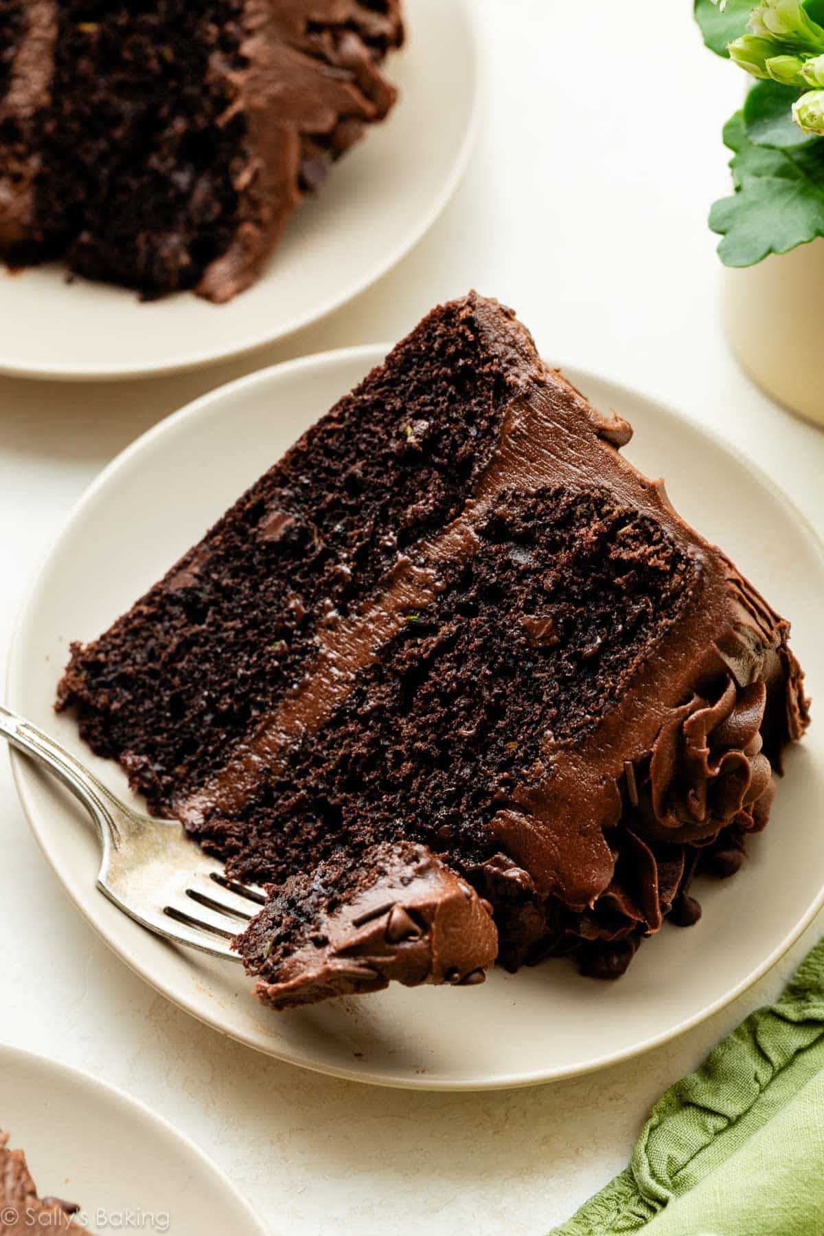 slice of chocolate zucchini cake with chocolate frosting on beige plate.