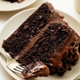 slice of chocolate zucchini cake with chocolate frosting on beige plate.