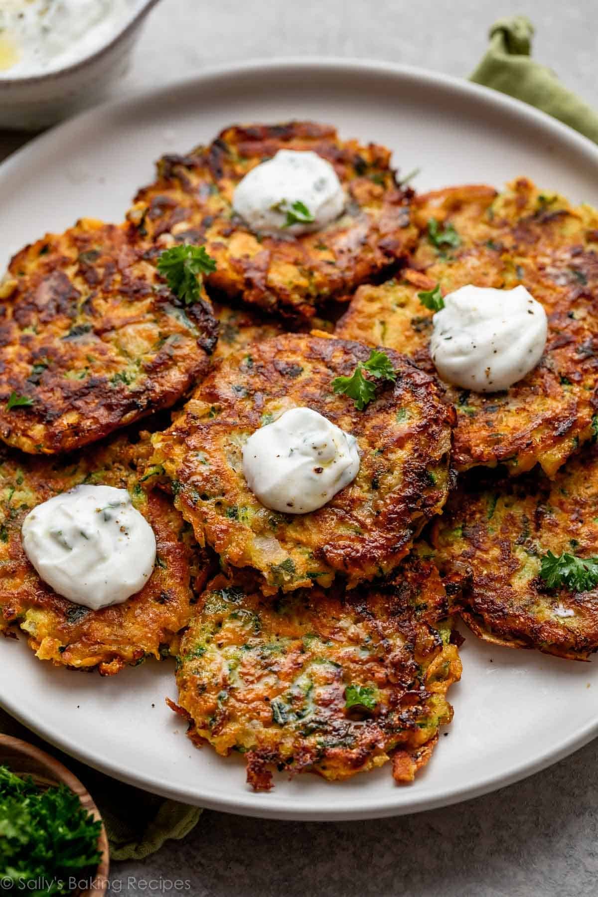 plate of zucchini sweet potato fritters with dollops of yogurt sauce on top of 4 of them.