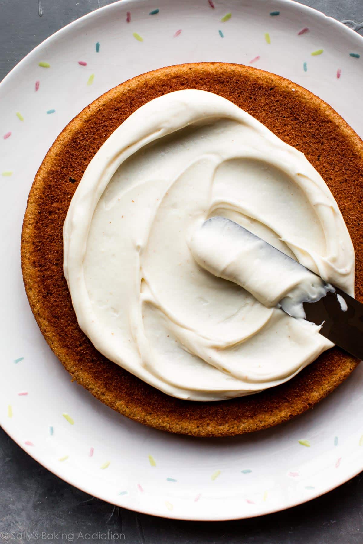 spreading brown butter cream cheese frosting onto layer of banana cake on a plate