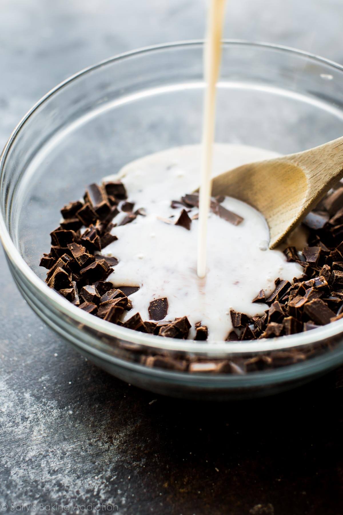 pouring warm coconut milk into glass bowl of chopped chocolate