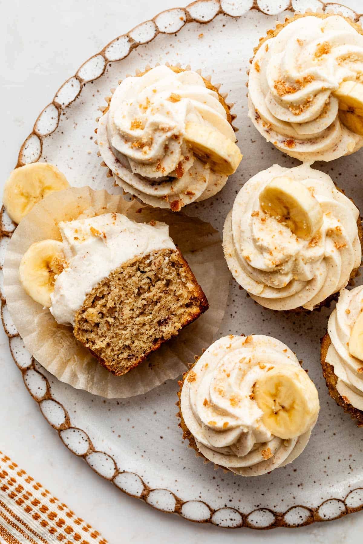 banana cupcakes with cinnamon cream cheese frosting, banana slice, and crushed nilla wafers on plate.
