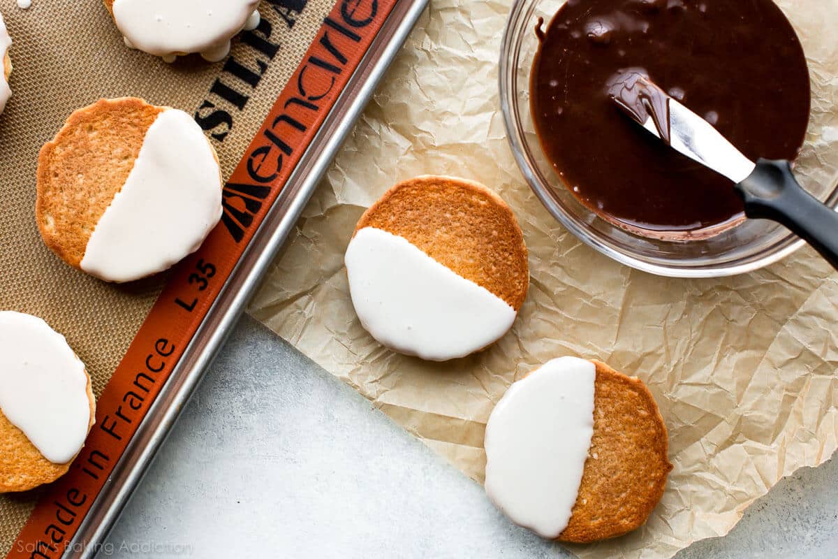 cookies with vanilla icing on half and a glass bowl of chocolate icing