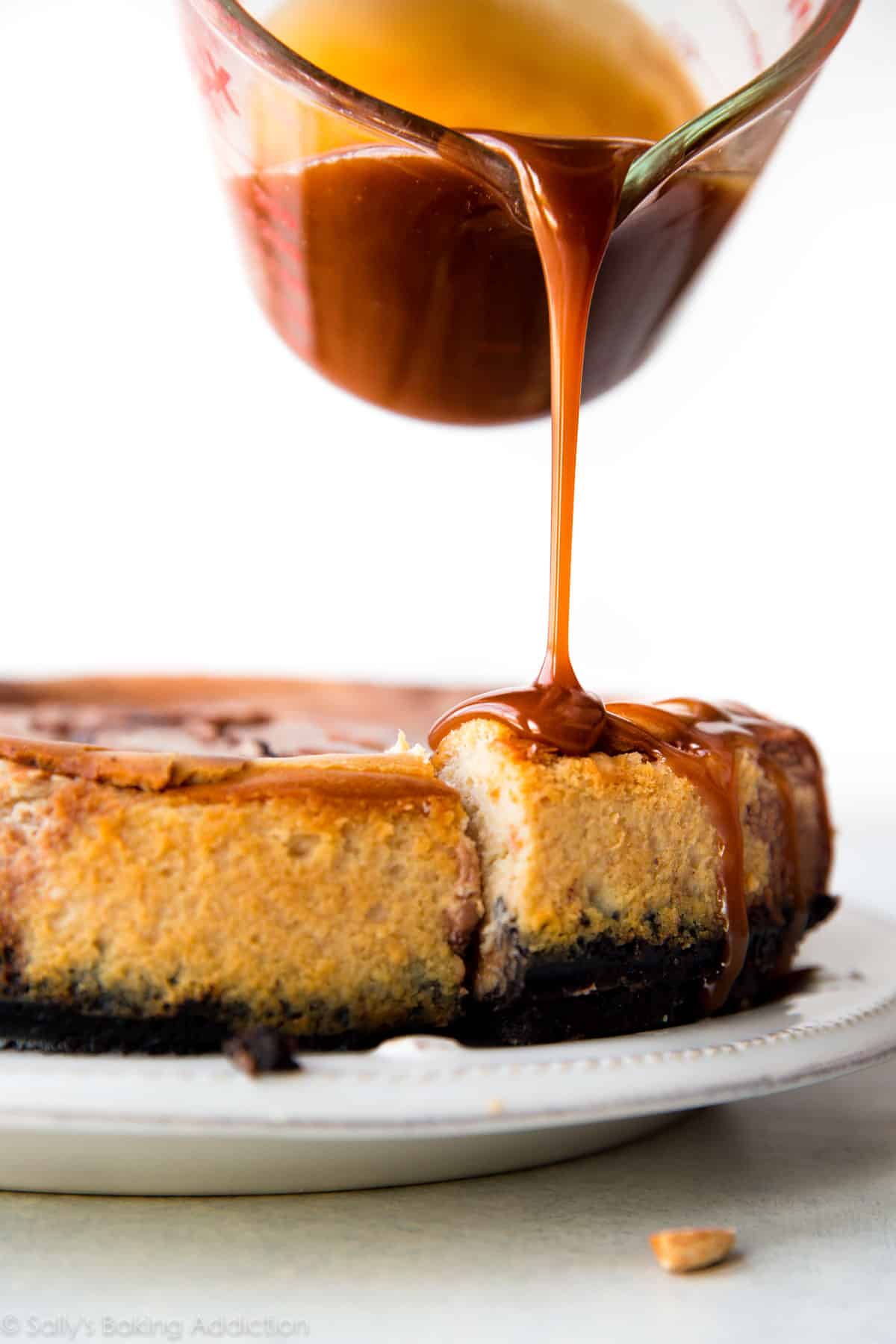 pouring salted caramel sauce onto Snickers cheesecake on a white plate