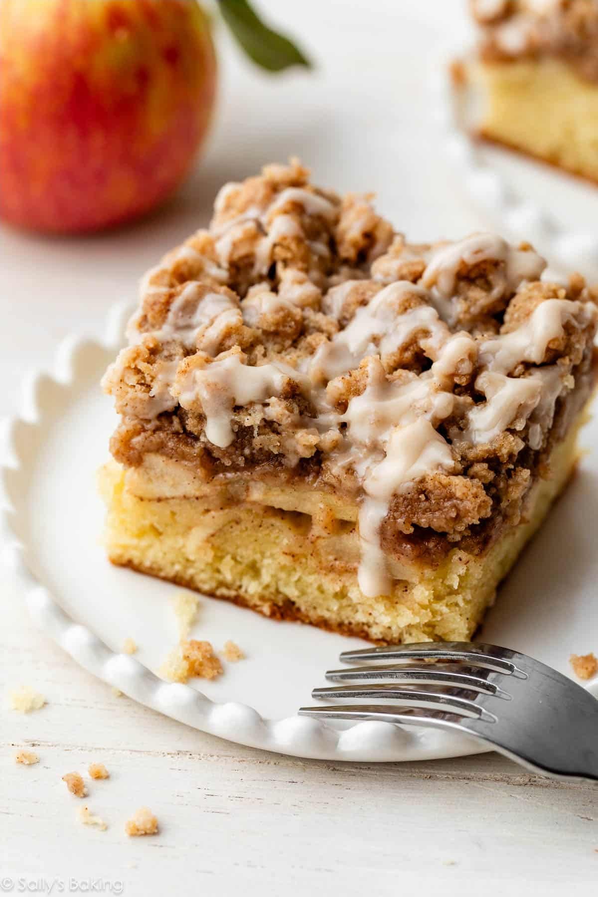 apple crumb cake with icing on top on small white plate.