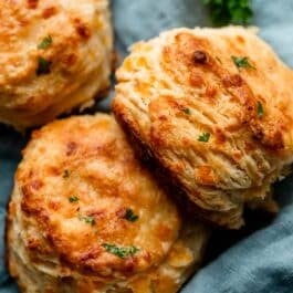 flaky cheddar biscuits on blue linen with fresh parsley sprinkled on top.