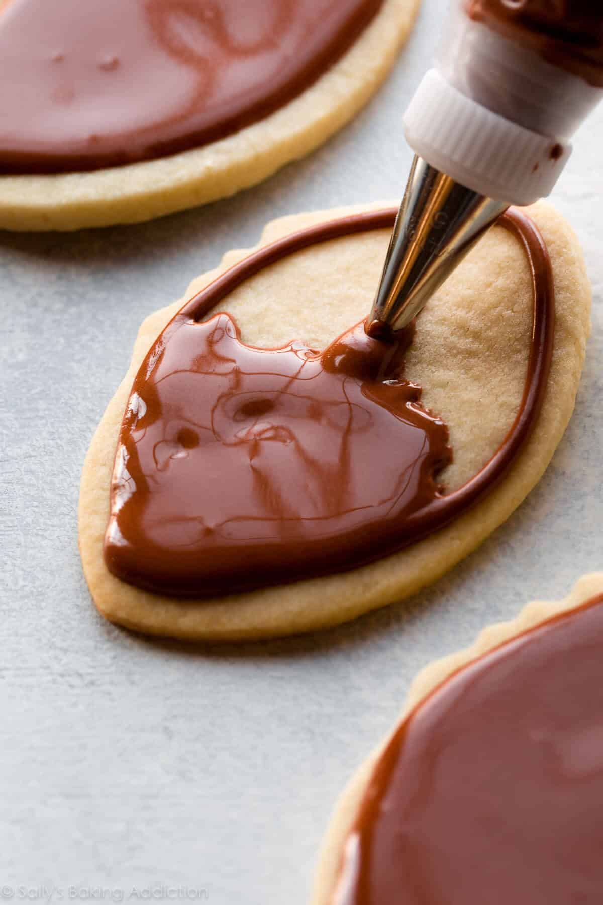 piping brown icing onto football sugar cookies