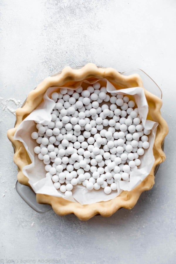 pie dough in a glass pie dish with pie weights on top