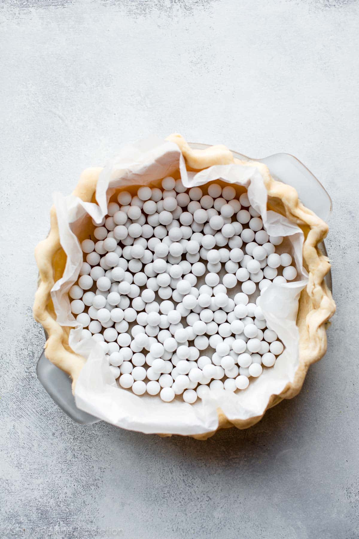 pie dough in a pie dish before baking with pie weights on top