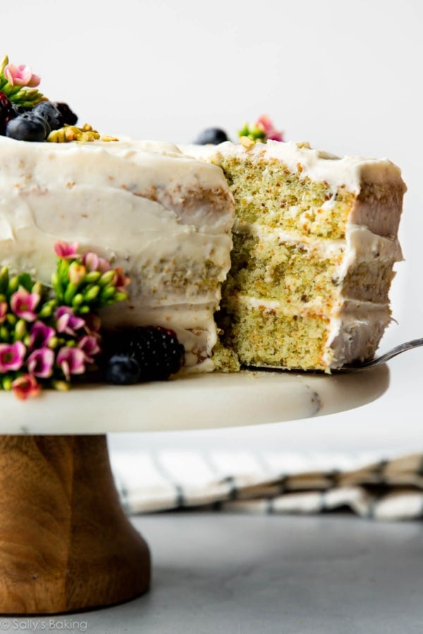 pistachio cake on a wood and marble cake stand with a slice on a cake server