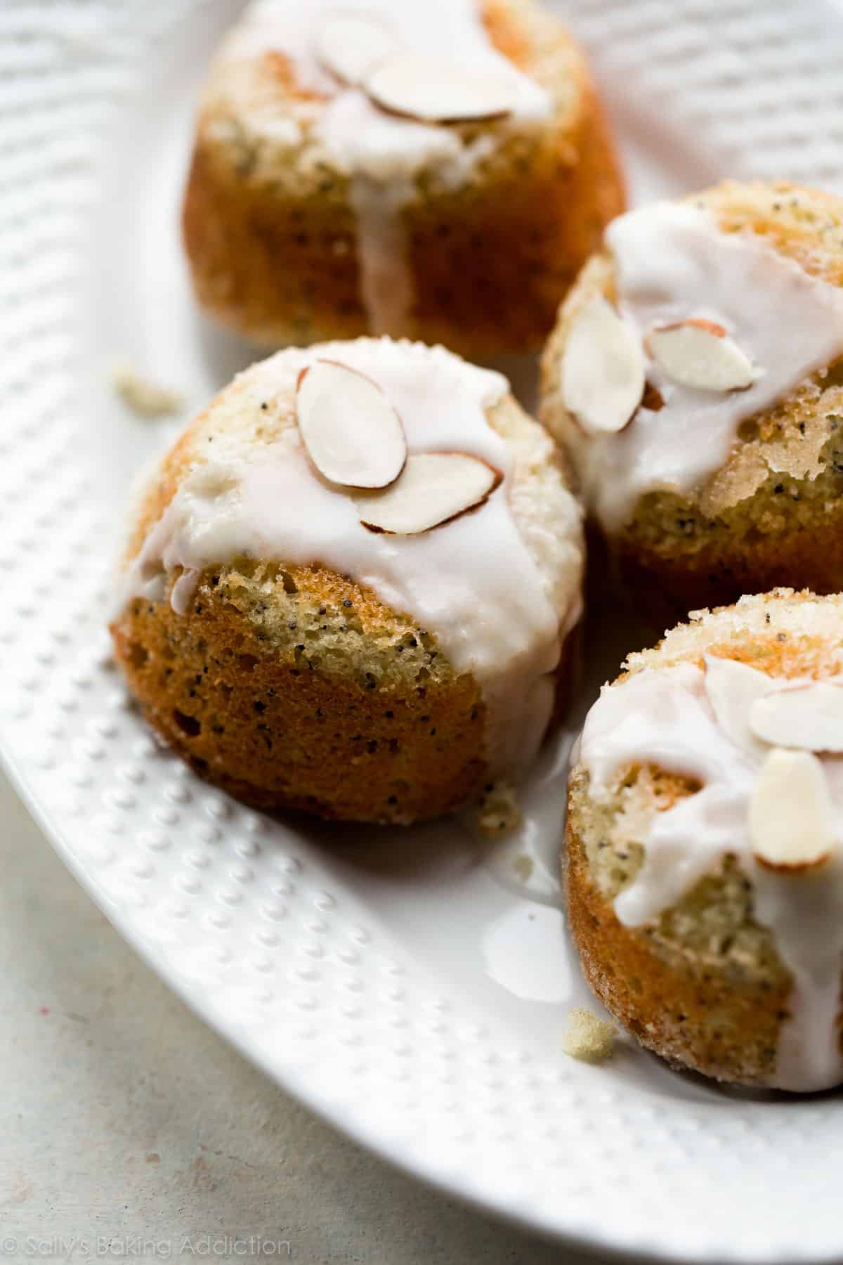 almond poppy seed tea cakes with icing and almond garnish on a white serving tray