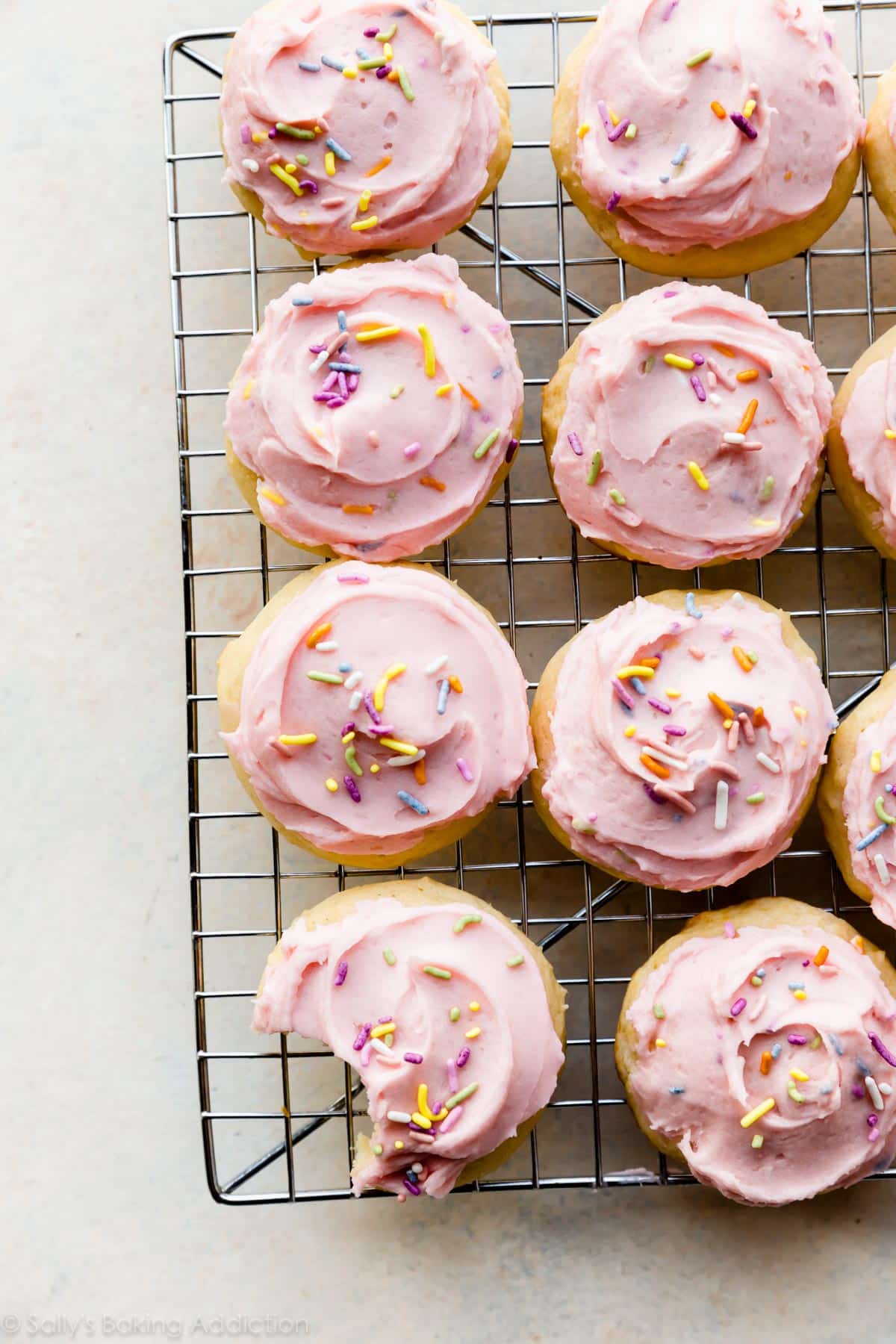 sugar cookies topped with pink buttercream and sprinkles on a cooling rack