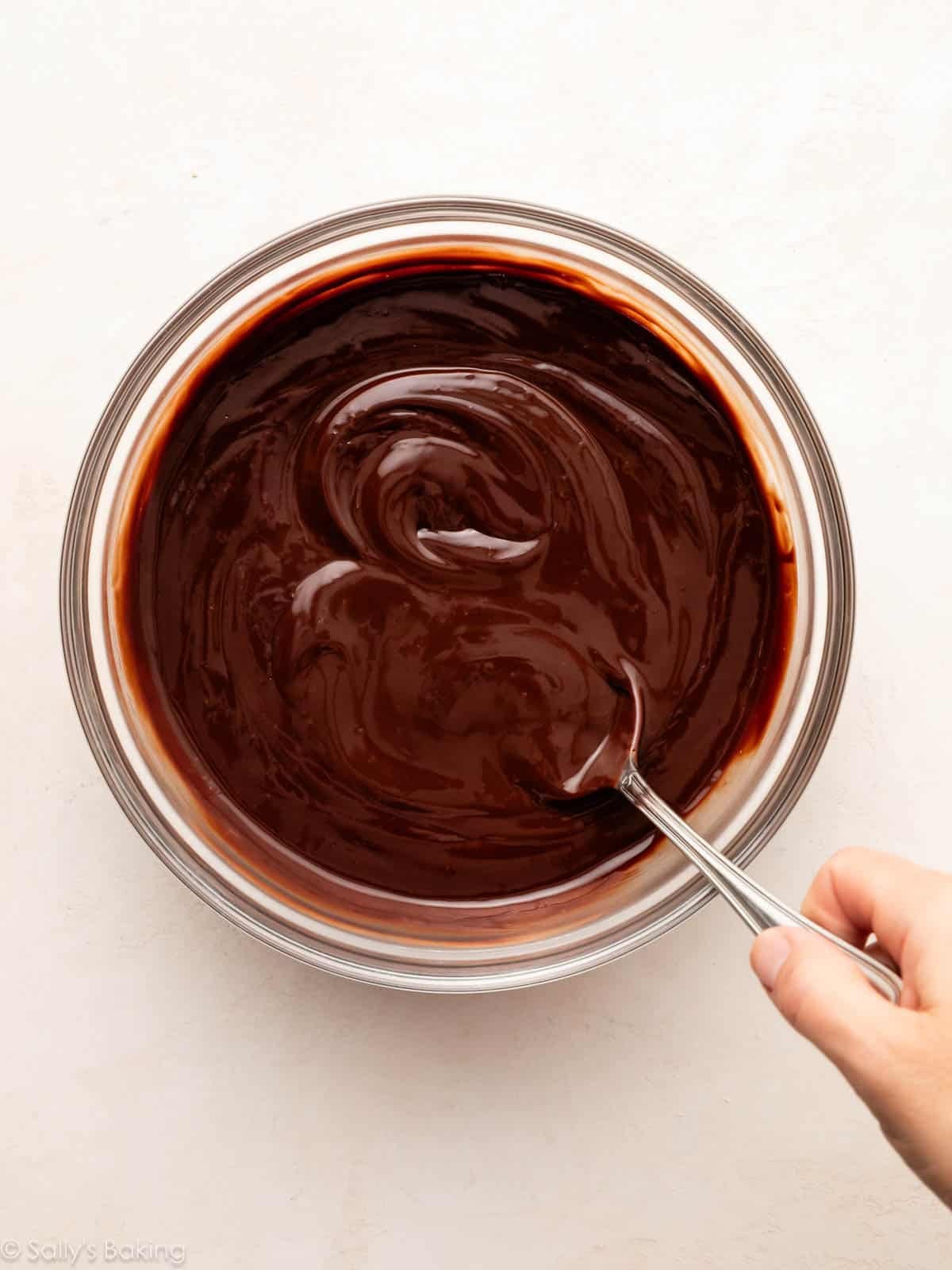 spoon stirring chocolate ganache in glass bowl.