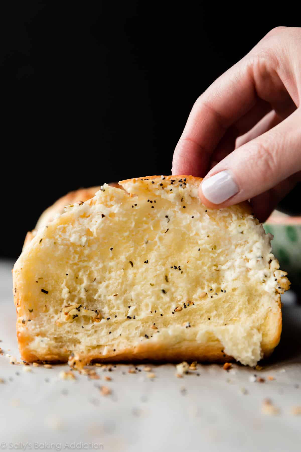 side view of everything bagel pull apart bread with a hand taking a slice