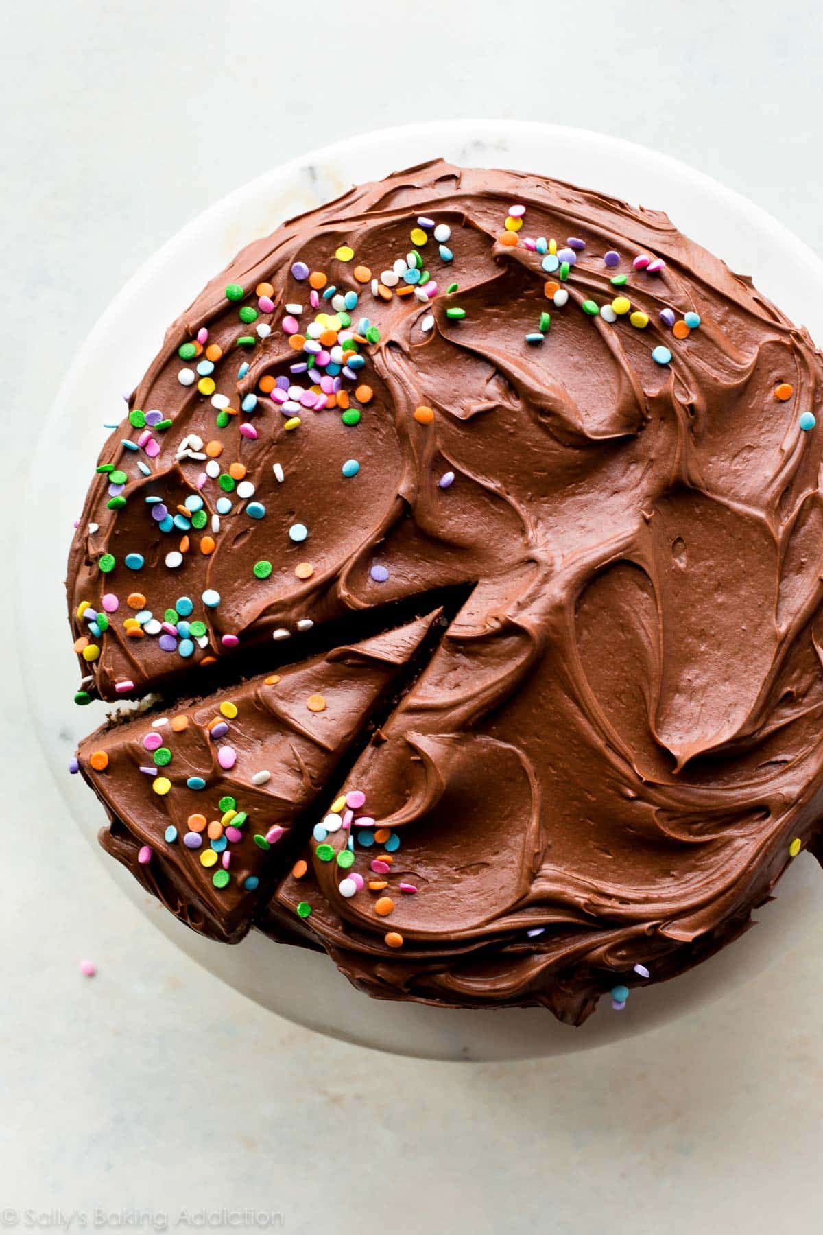overhead image of cake with chocolate cream cheese frosting and sprinkles on a marble cake stand