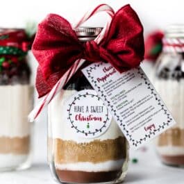 glass jar with ingredients for cookies decorated with ribbon and a recipe card