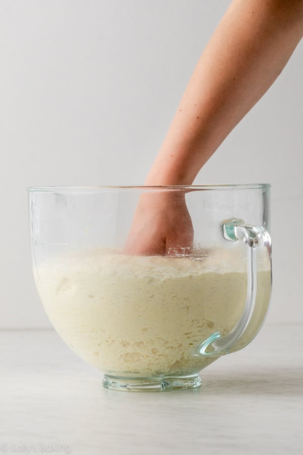 hand punching down dough in glass bowl.