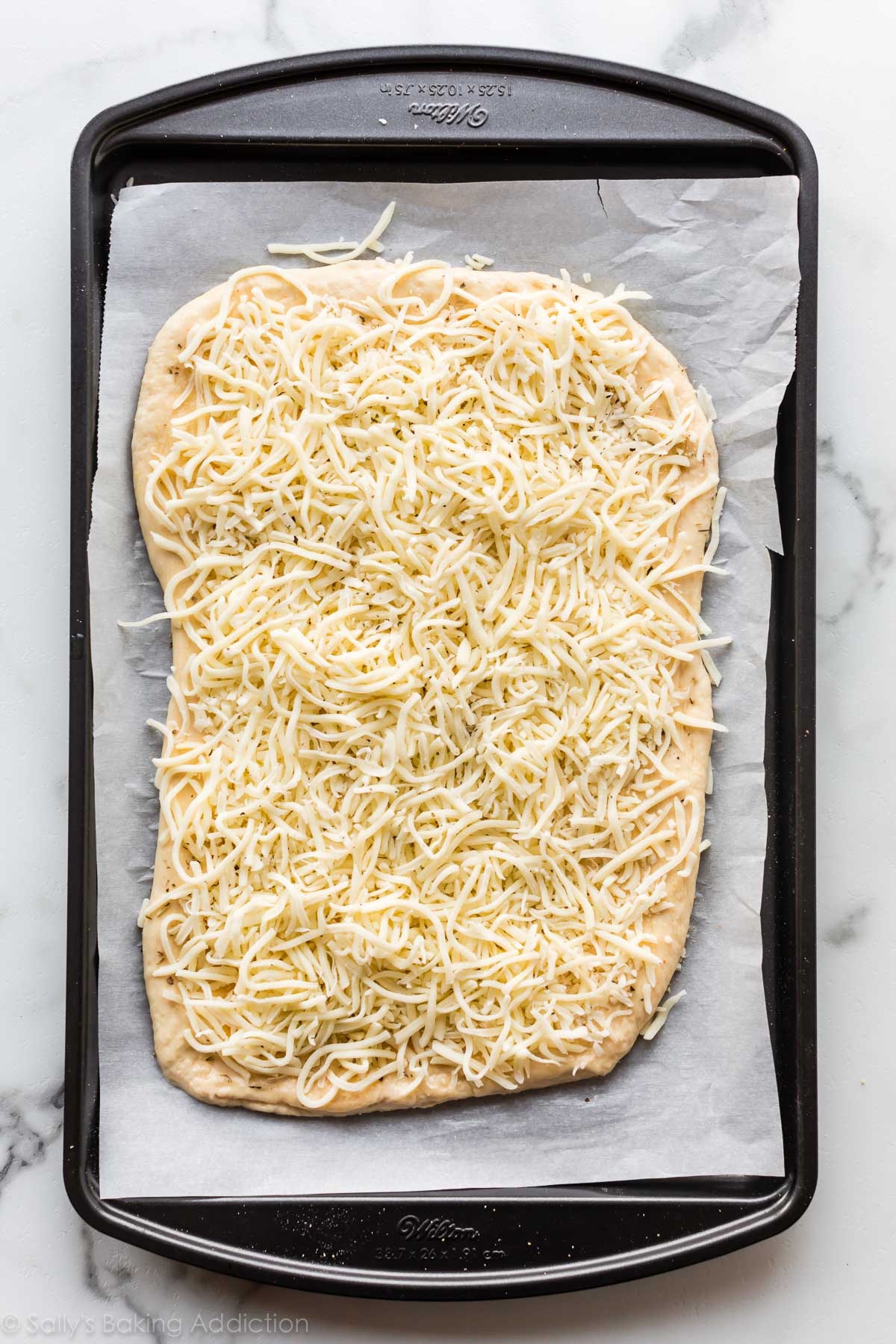 Homemade pizza dough with cheese on top on a parchment lined baking sheet