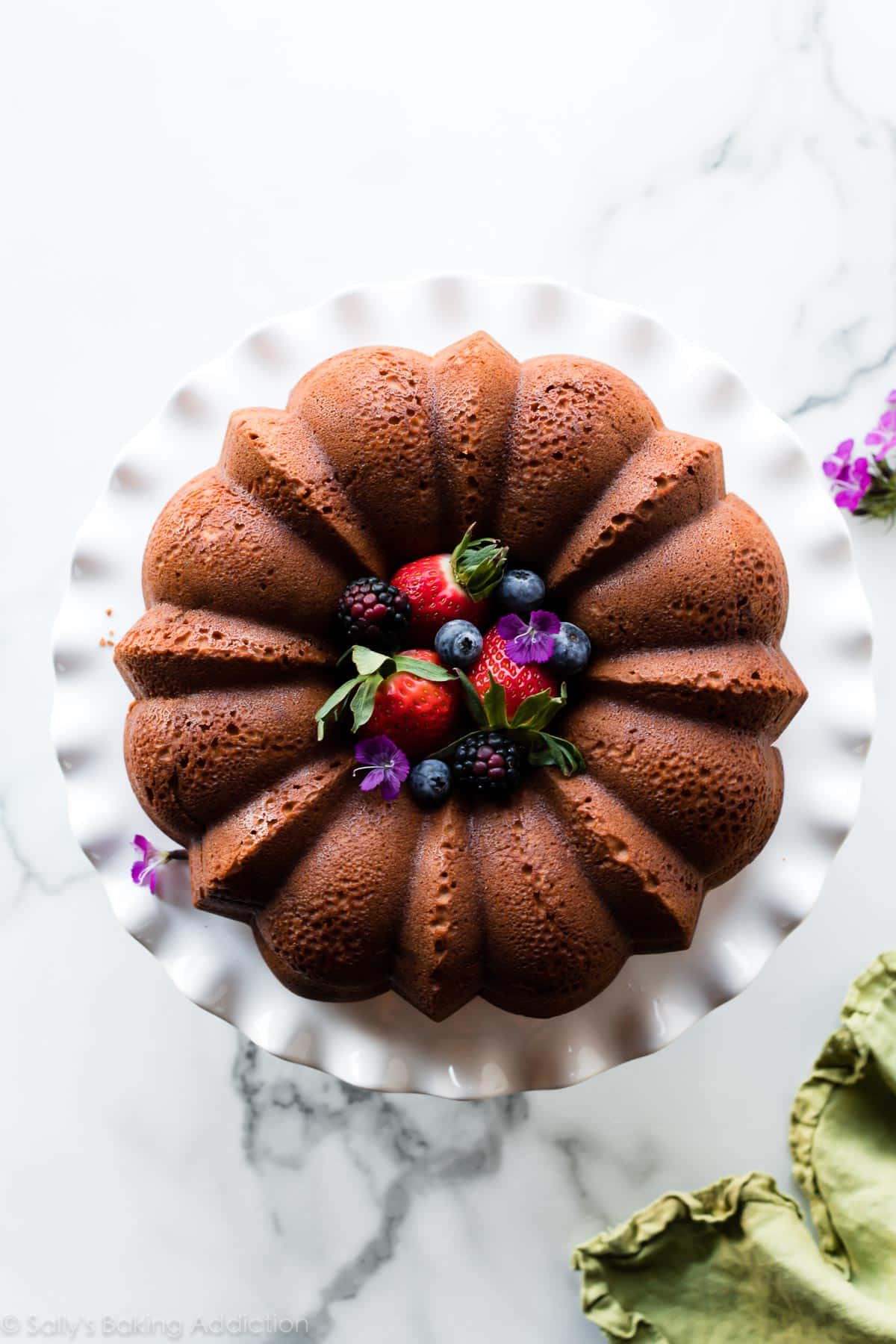 overhead image of cream cheese pound cake on white ruffled cake stand with berries in the center