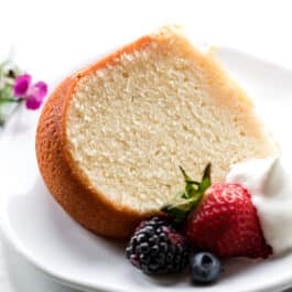 slice of cream cheese pound cake on a white plate with whipped cream and berries