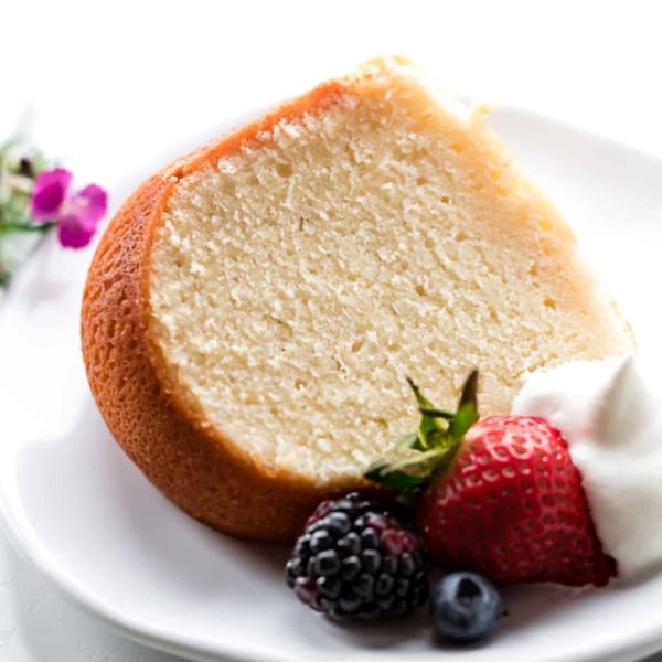 slice of cream cheese pound cake on a white plate with whipped cream and berries
