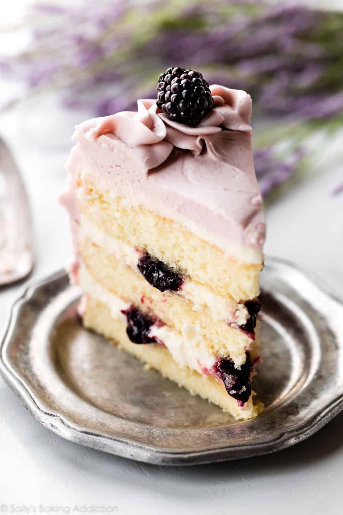 Slice of lavender butter cake on a silver plate with purple frosting and blackberry jam