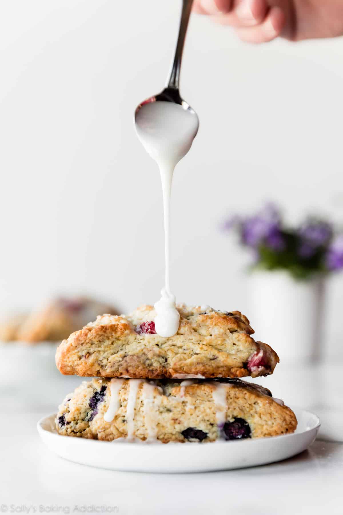 Drizzling vanilla icing on stack of scones on a white plate