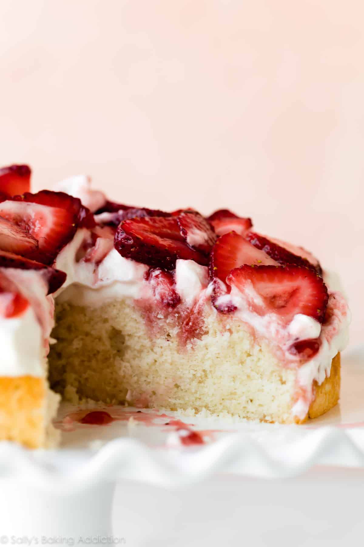 One layer vanilla cake topped with whipped cream and juicy strawberries on white cake stand