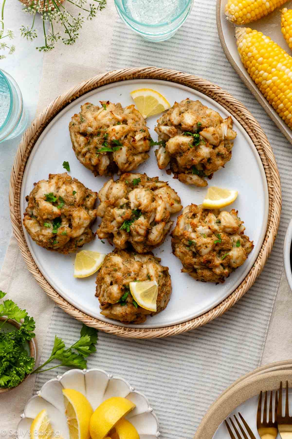 crab cake meal on table with corn on the cob, roasted potatoes, and glasses of water.