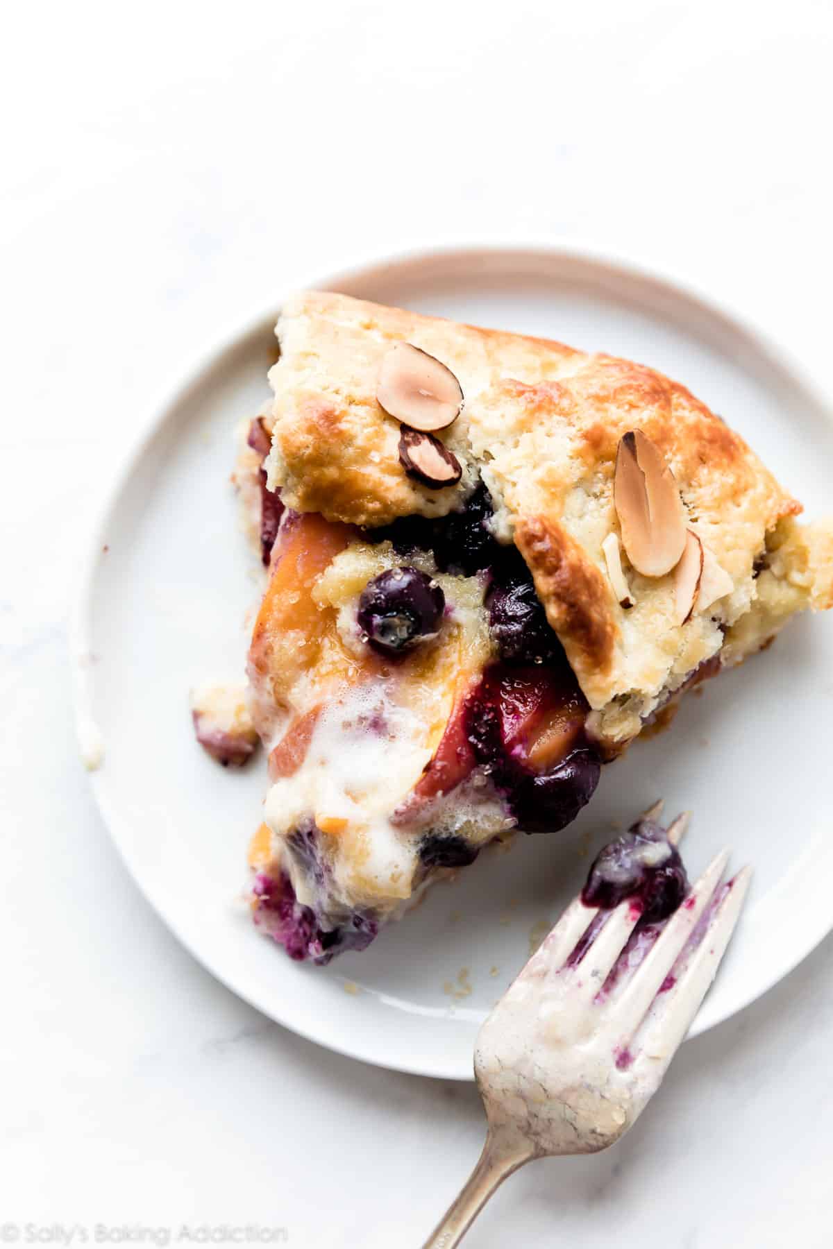 Slice of blueberry peach frangipane galette on white plate