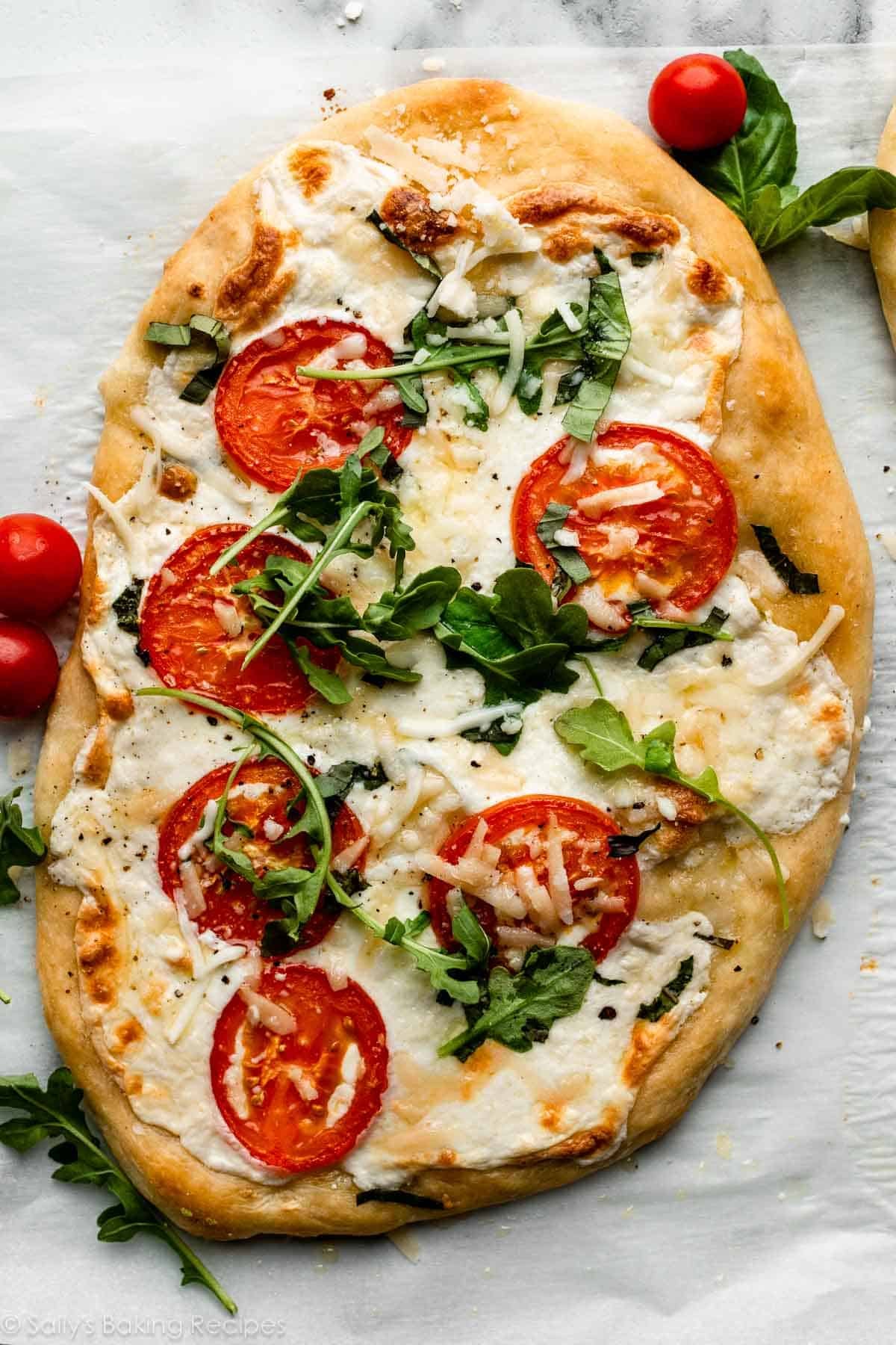 homemade flatbread pizza with mozzarella cheese, tomatoes, and arugula on top.