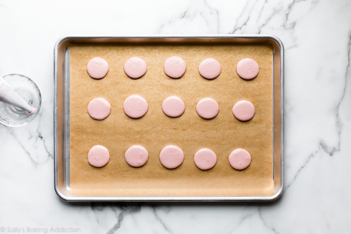 piped macaron shells on lined baking sheet before baking