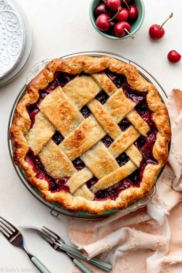 homemade cherry pie with lattice crust on top with pink linen and fresh cherries.