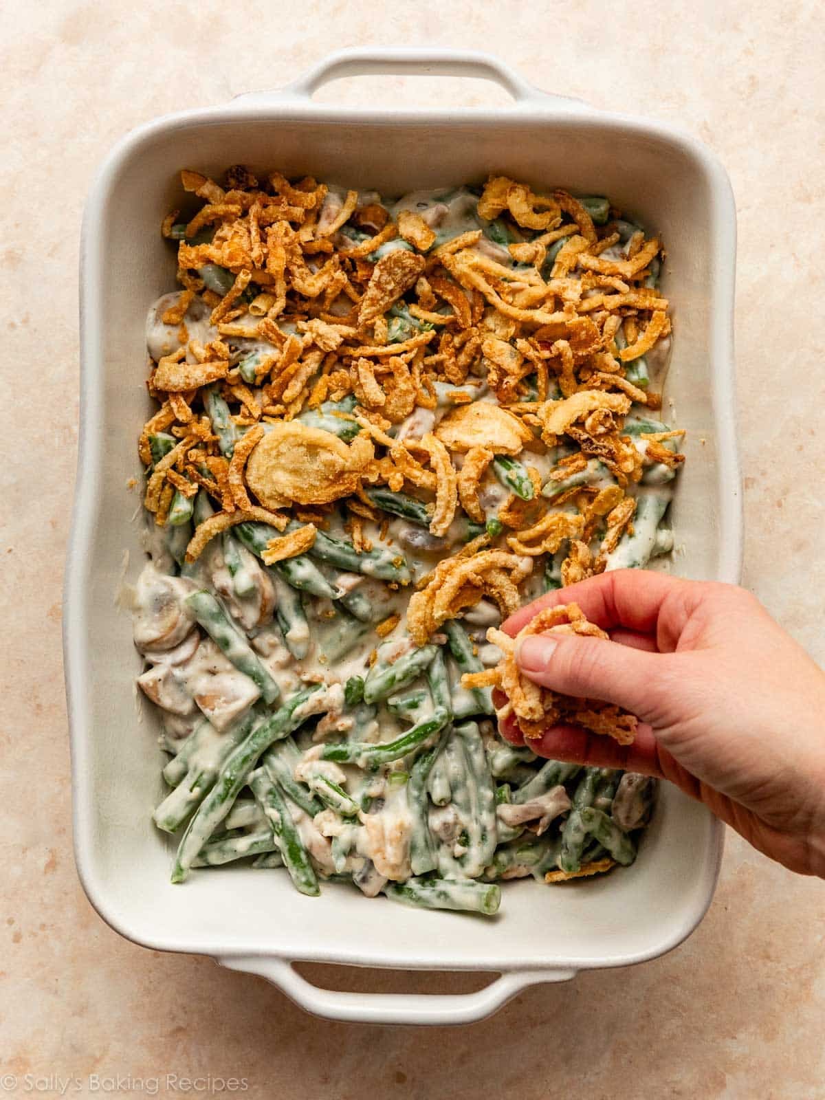 hand sprinkling French's crispy fried onions on top of green beans.