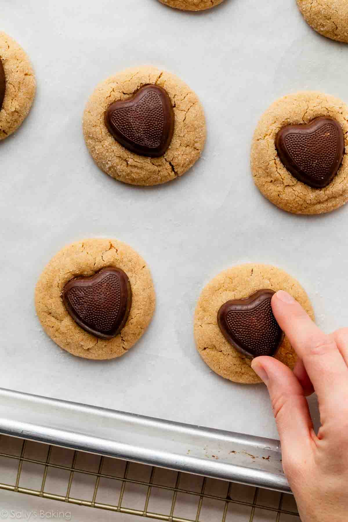 hand pressing a chocolate heart candy into the top of a cookie.