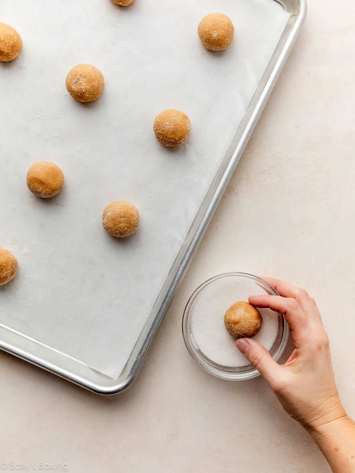 hand rolling cookie dough in small bowl of sugar.