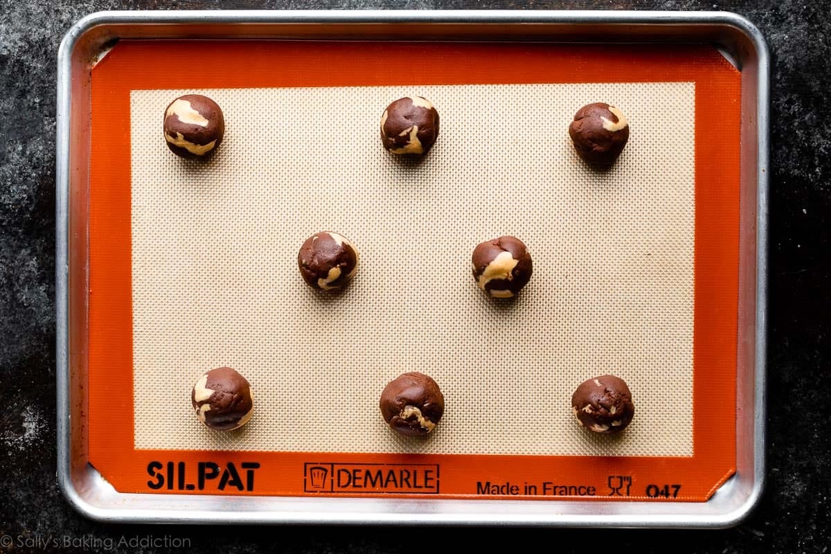chocolate dough balls swirled with peanut butter on lined baking sheet