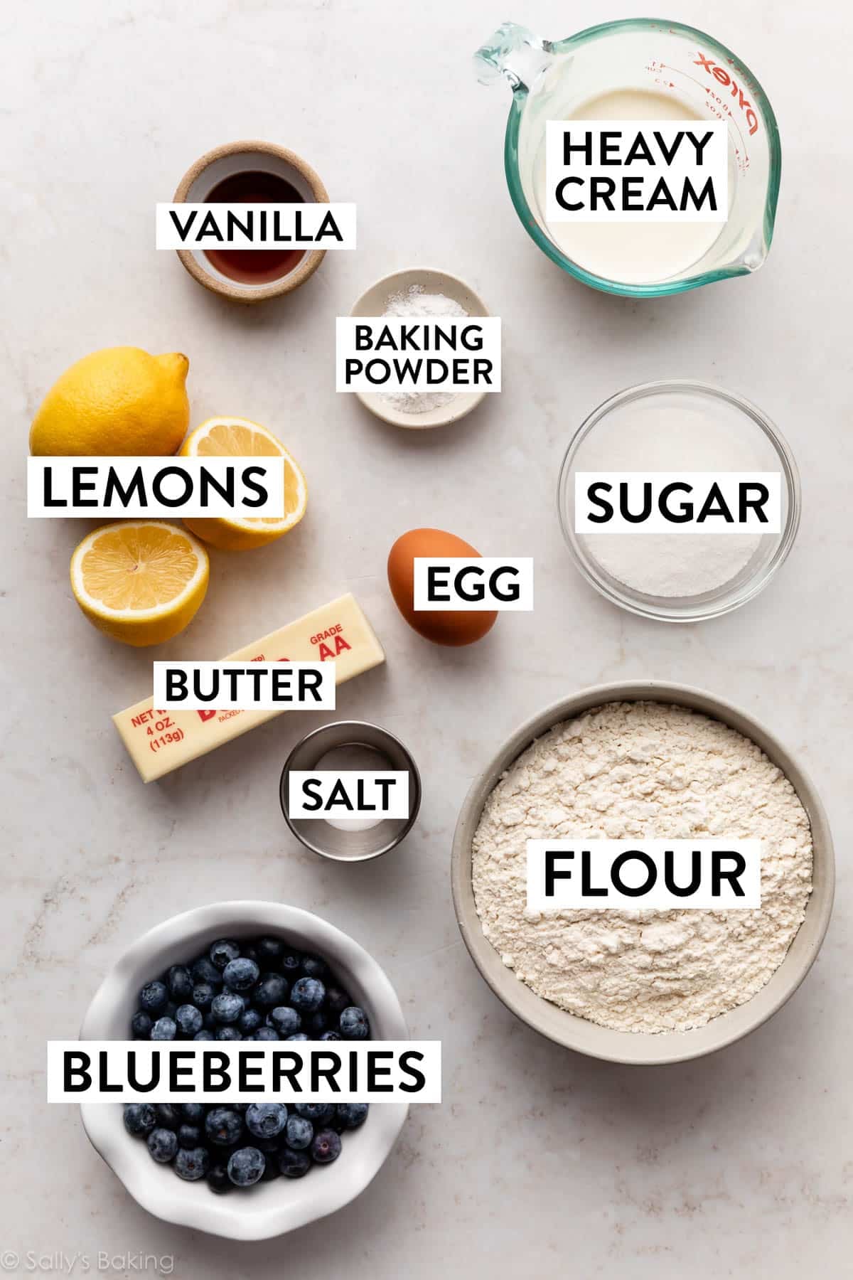 ingredients on marble surface including butter, flour, cream, sugar, egg, and lemons.