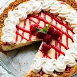 whipped cream and raspberry sauce topped cheesecake pie with 1 slice removed.