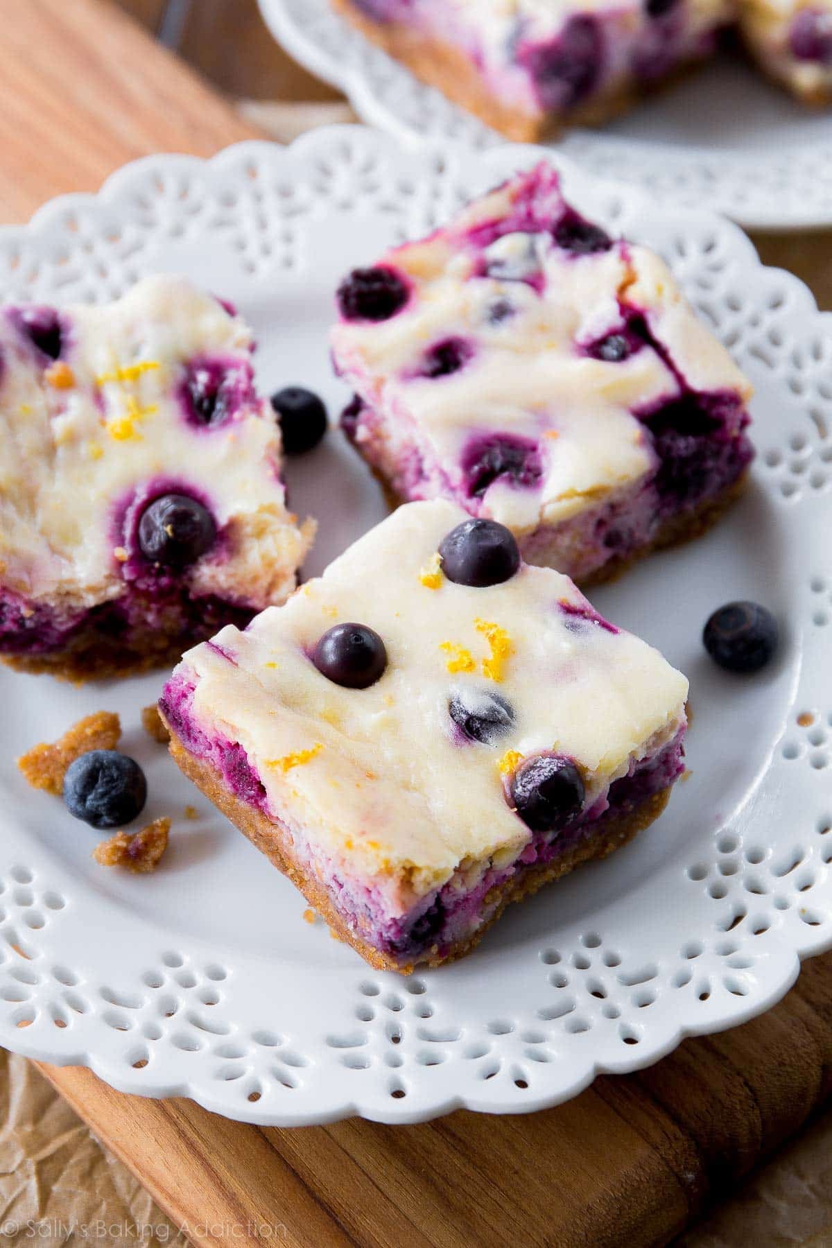 3 lemon blueberry cheesecake bars with graham cracker crust on white plate.
