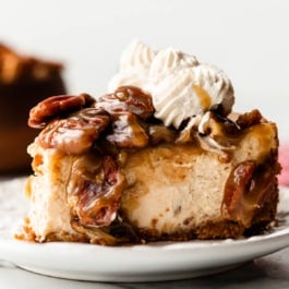 slice of brown sugar pecan pie cheesecake with gooey caramel topping and whipped cream piped on top.