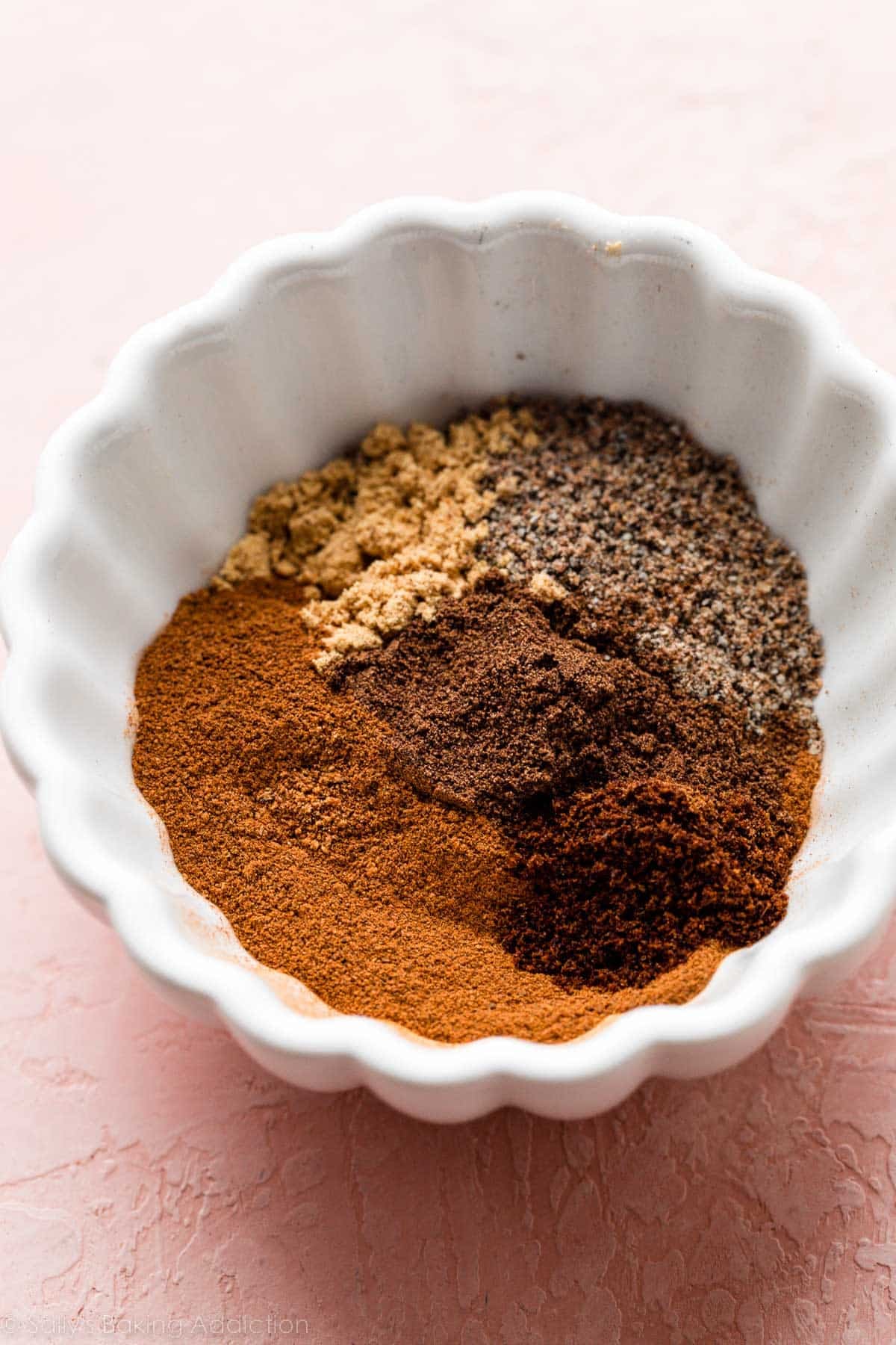 white ramekin bowl of mixed spices on pink backdrop.