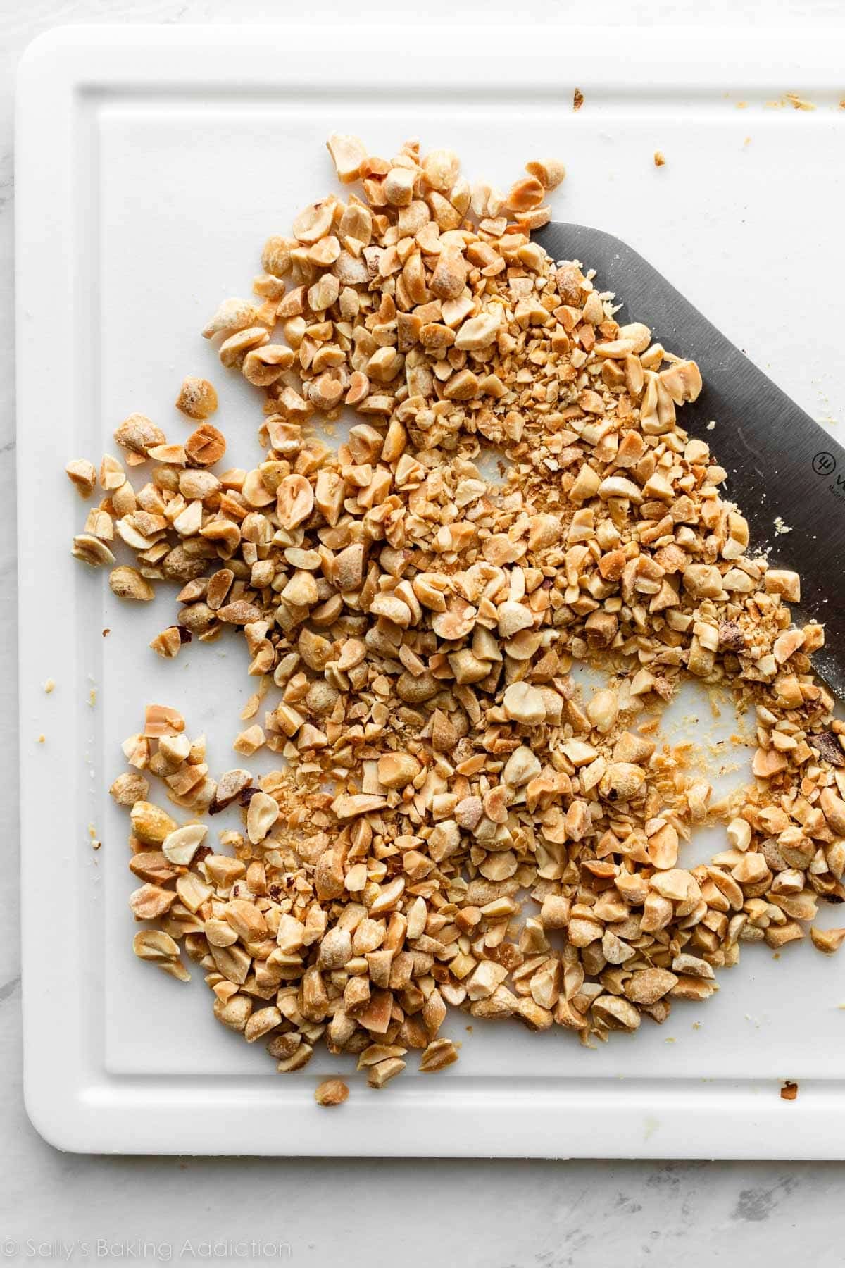chopped peanuts on white cutting board.