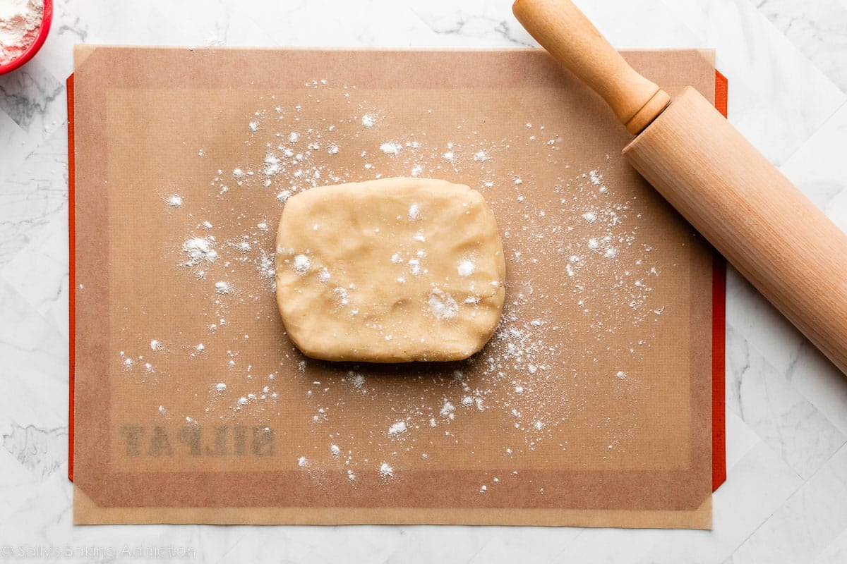 block of vanilla dough on parchment paper with rolling pin next to it.